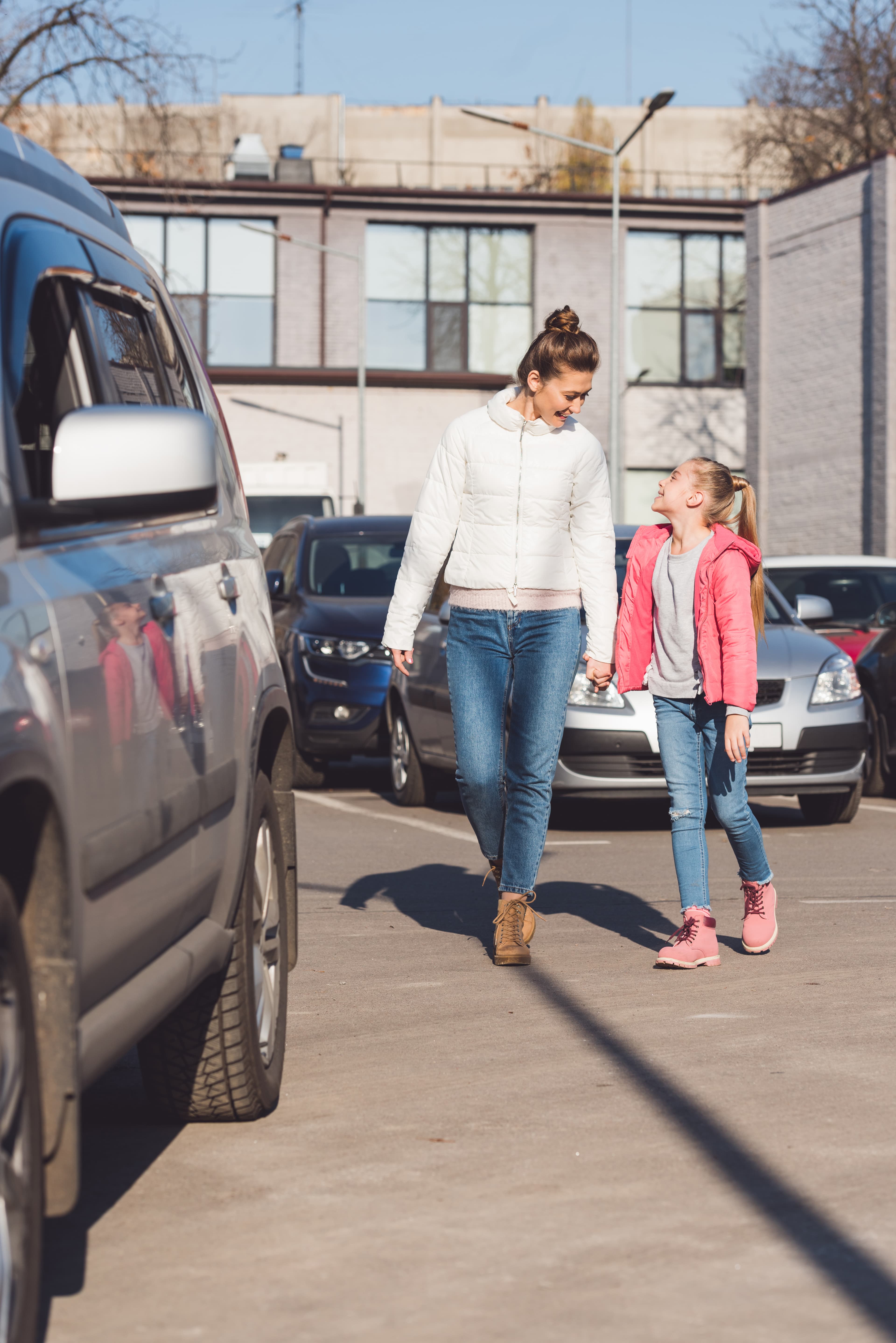 A mother and daughter walking hand in hand through a school parking lot