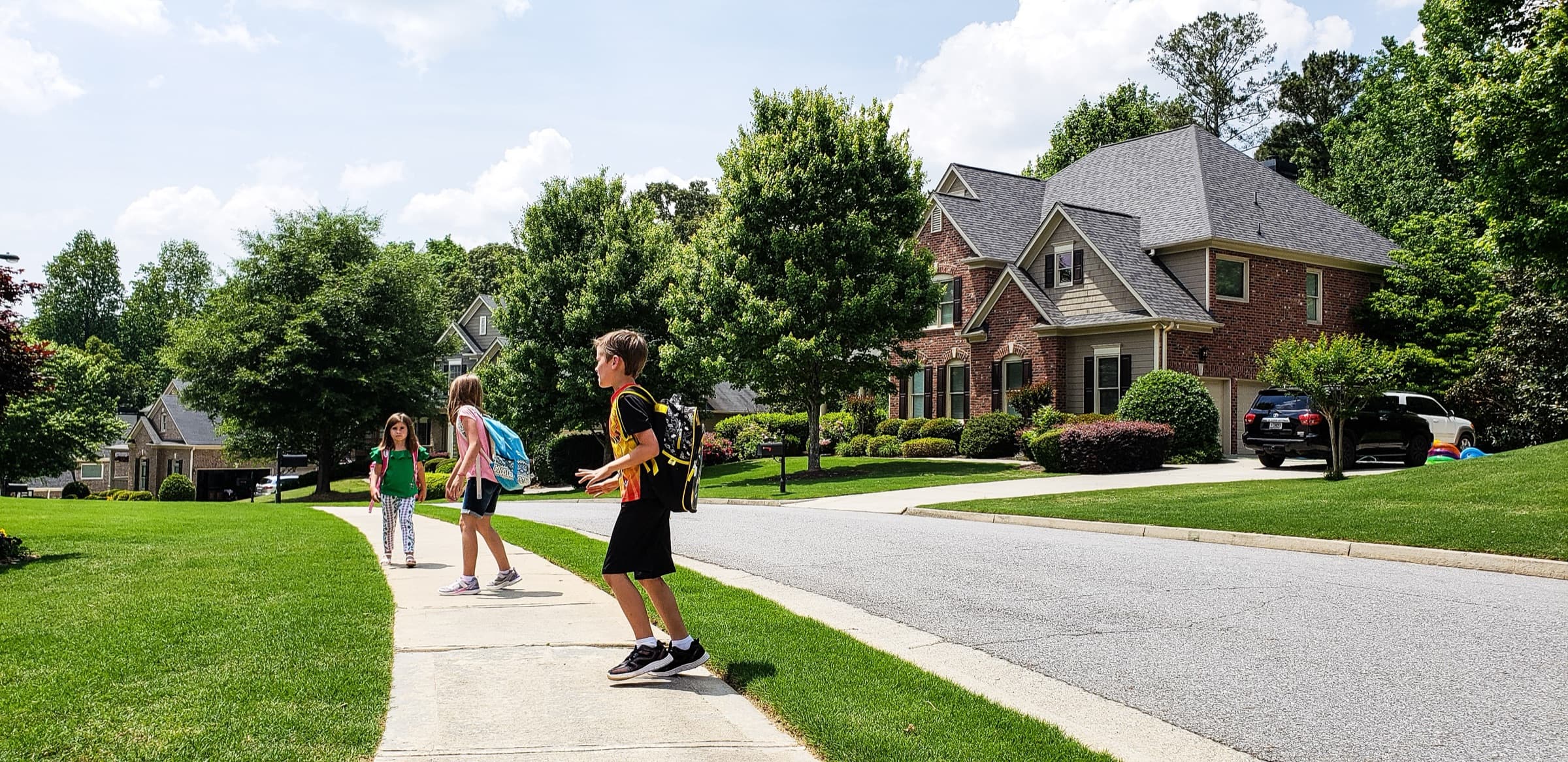 Children with backpacks walking to school along a sidewalk in a suburban neighborhood of family homes